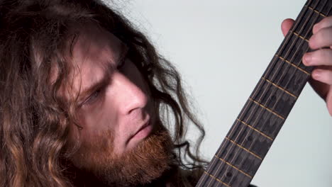 cabello largo, barba, hombre de color marrón tocando la guitarra acústica, fondo claro blanco.