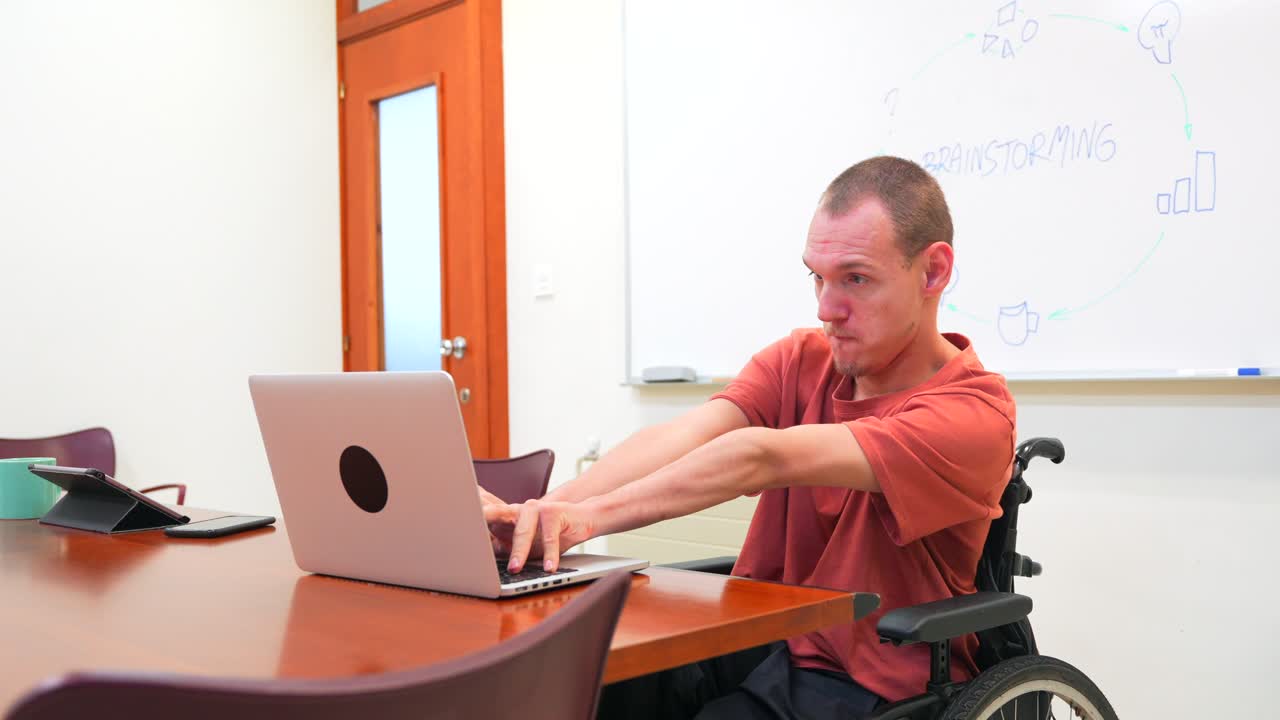 Man in wheelchair working on laptop in meeting room