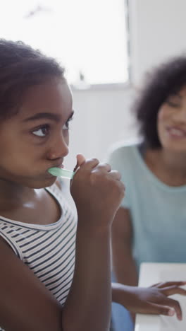 vertical video of biracial mother and daughter brushing teeth in bathroom, slow motion