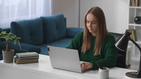 Una-Mujer-Joven-Está-Trabajando-Con-Una-Computadora-Portátil-En-La-Sala-De-Estar-Navegando-Por-Internet-Con-Un-Portátil-Moderno-Usando-Redes-Sociales-En-La-Oficina-Del-Hogar