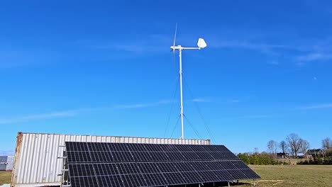 a small wind turbine and a solar panel in a green field, shipping container, under a clear blue sky