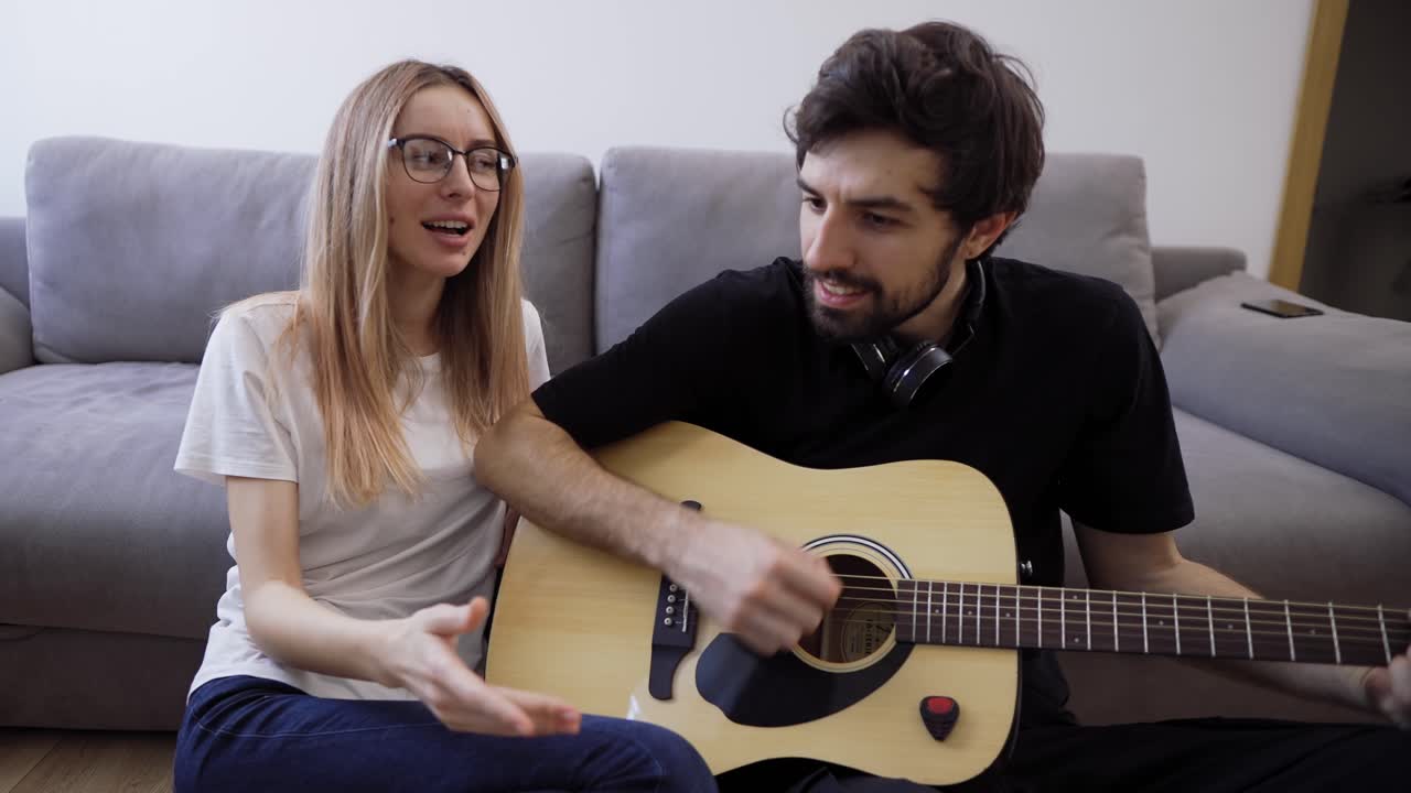 hombre con auriculares toca la guitarra en casa, cantando felizmente con su novia