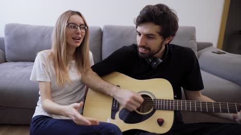 Man-in-headphones-plays-the-guitar-at-home,-happily-singing-with-his-girlfriend