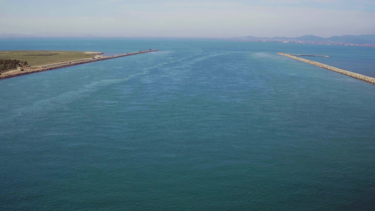 Il drone avanza attraverso un canale portuale, con il mare aperto che si estende davanti.