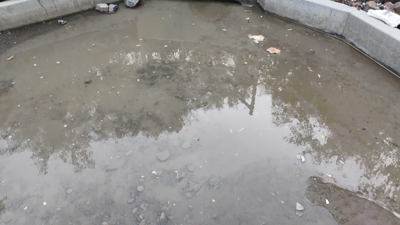 Concrete culvert channeling stormwater runoff, overcast daylight, steady camera, rocky riprap environment