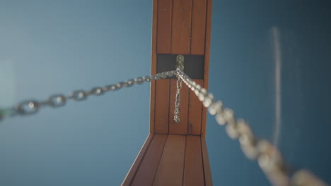 close-up of a metallic chain attached to wooden frame, captured from a low angle against a bright blue sky, showcasing industrial strength and natural materials blending with outdoor scenery