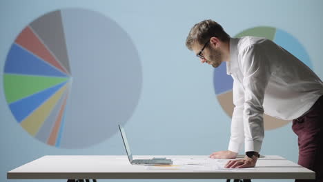 a young man stands at a table and looks at the graphs lying on the table and conducts a brainstorming session. management of the company. work at night. creation and planning of the company's work