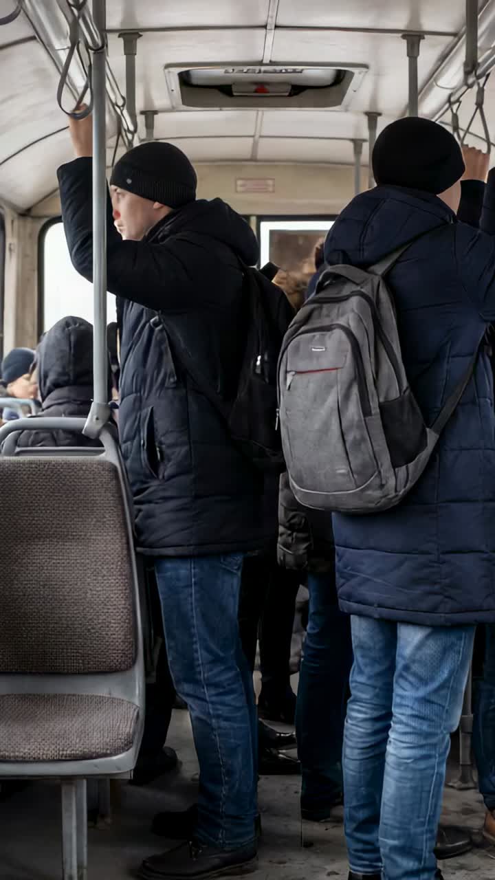 Vertical video: Holding poles, two men in winter coats steadying on moving bus, backpacks