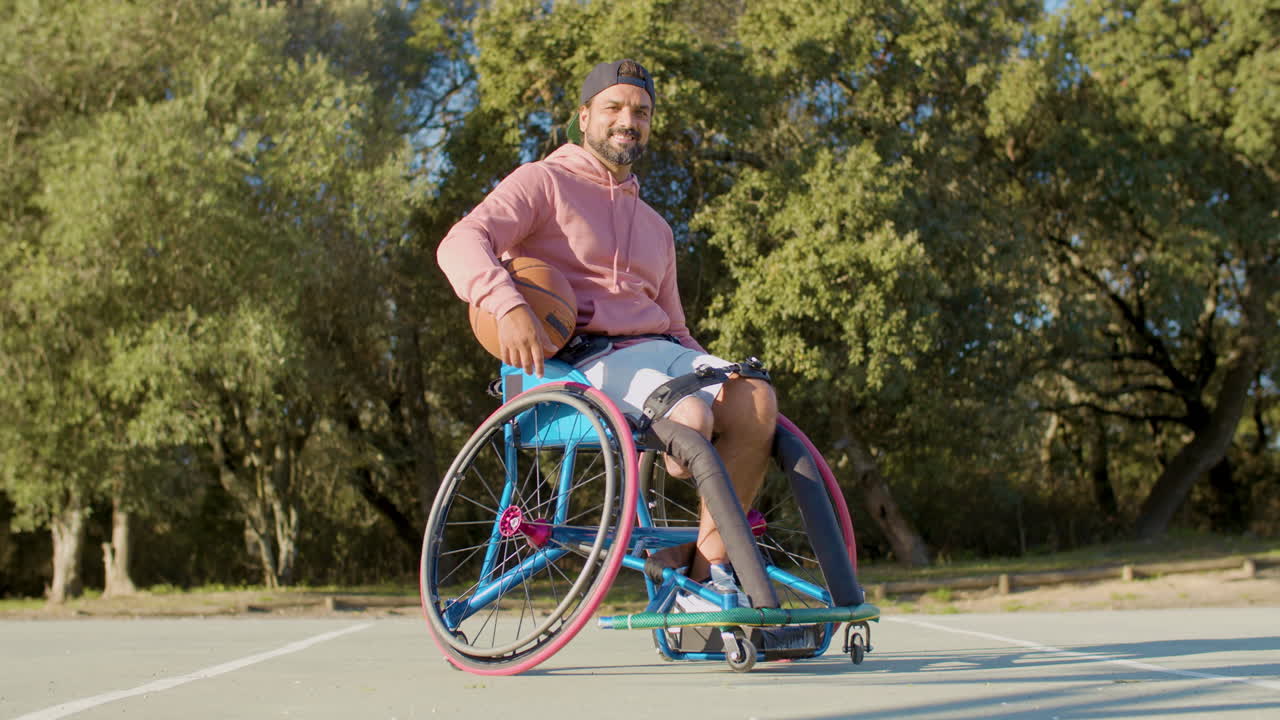 hombre barbudo feliz en silla de ruedas deportiva en la cancha de baloncesto