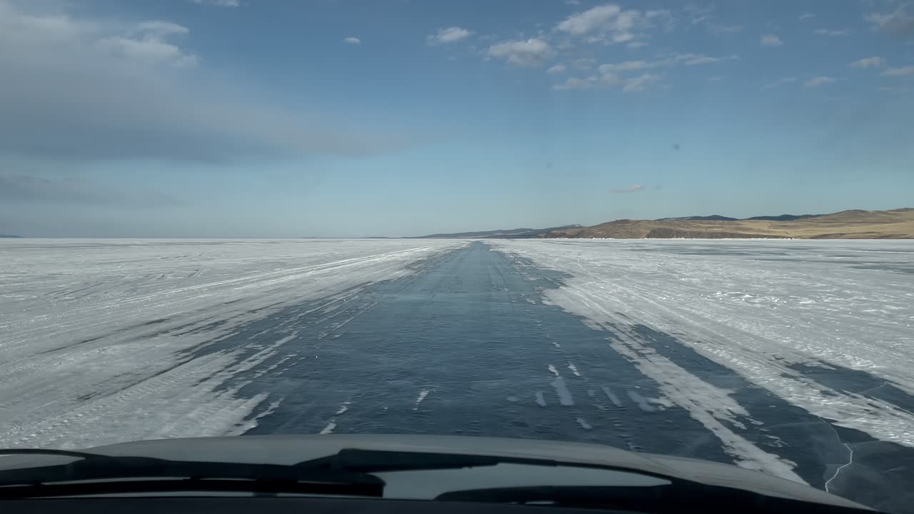 Filmato POV da un veicolo in movimento che percorre una strada di ghiaccio invernale sul lago ghiacciato Baikal, Oblast di Irkutsk, Russia, con superficie innevata e colline distanti.
