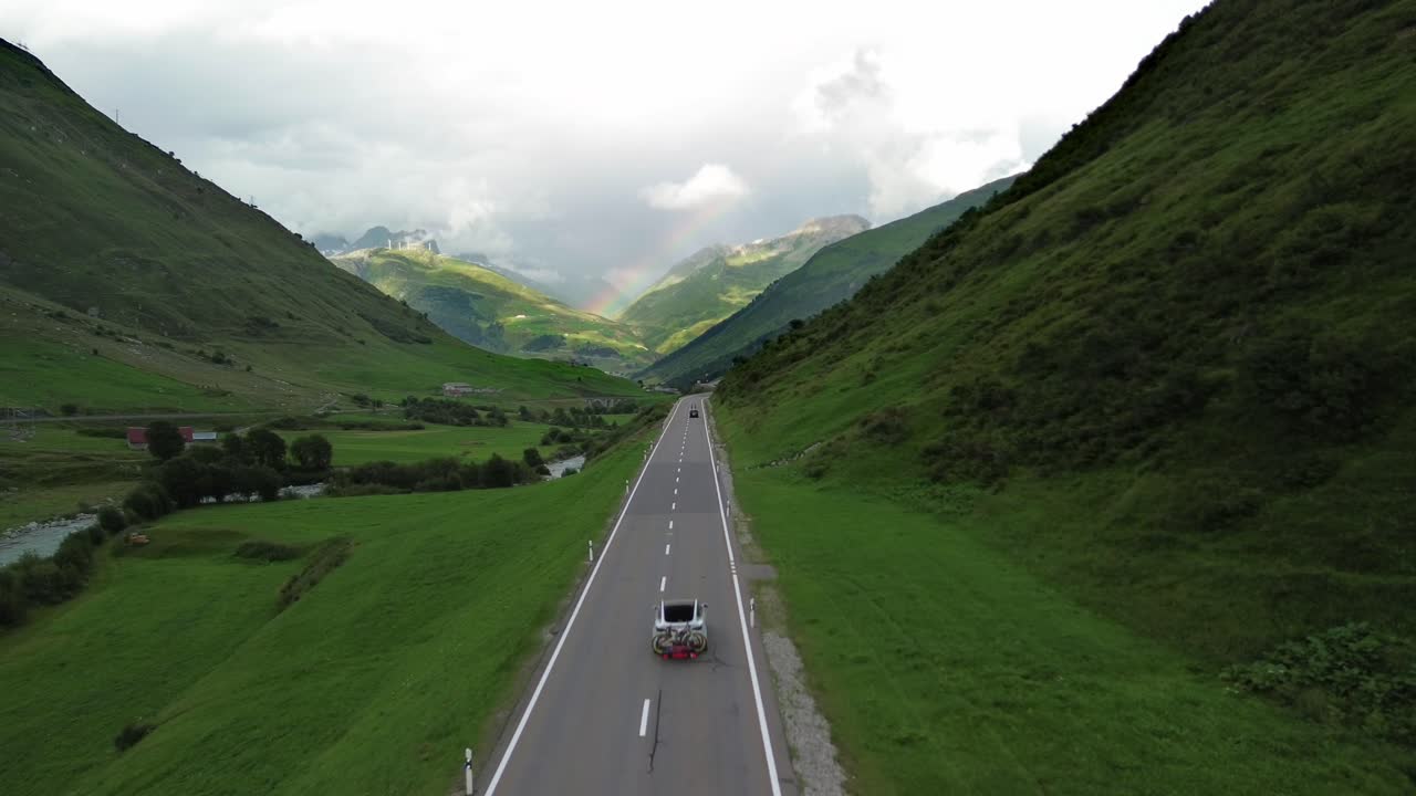 Road in Swiss Alps with cars and rainbow at the sky shot from a drone