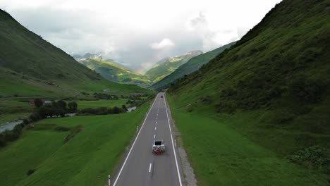 road in swiss alps with cars and rainbow at the sky shot from a drone