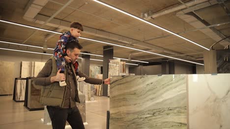 a young father with his son in his arms chooses ceramic tiles in a construction supermarket. a young father with his son in his arms chooses ceramic tiles in a construction supermarket. a collection of ceramic tiles for home renovation