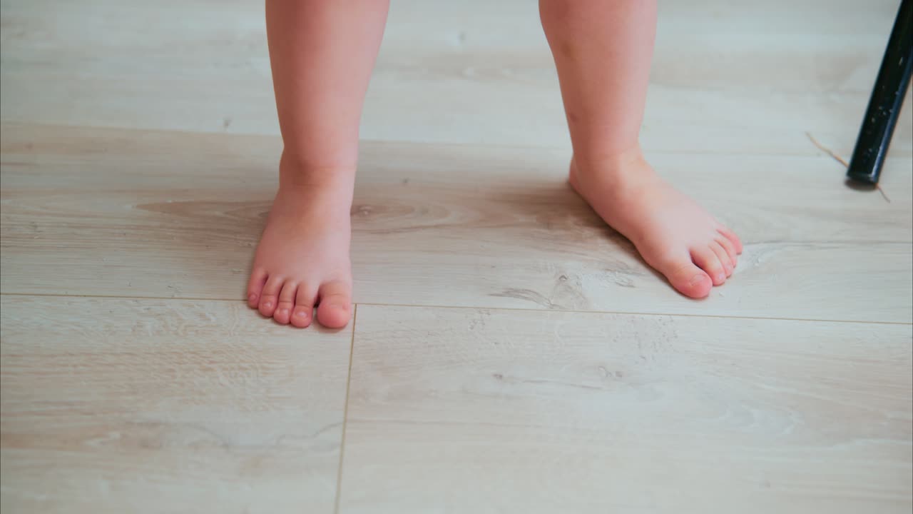A Close-Up View of a Child's Feet Standing on a Light-Colored Wooden Floor, Highlighting the Innocence of Early Steps and Playful Moments