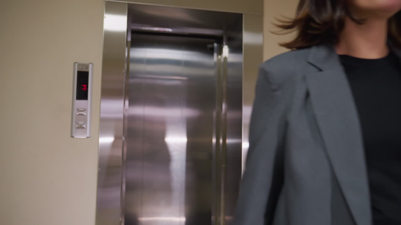Businesswoman walking out of elevator, dressed in gray suit, confident expression, modern office building, professional attire, career success, corporate setting, workday