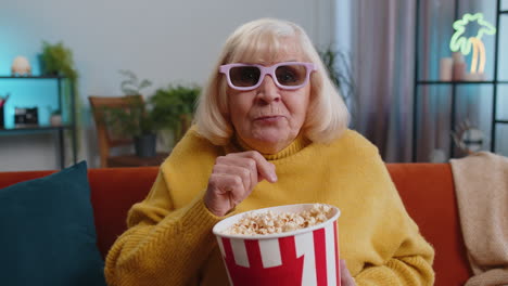 grandmother woman on couch eating popcorn watching interesting tv serial sport game online at home