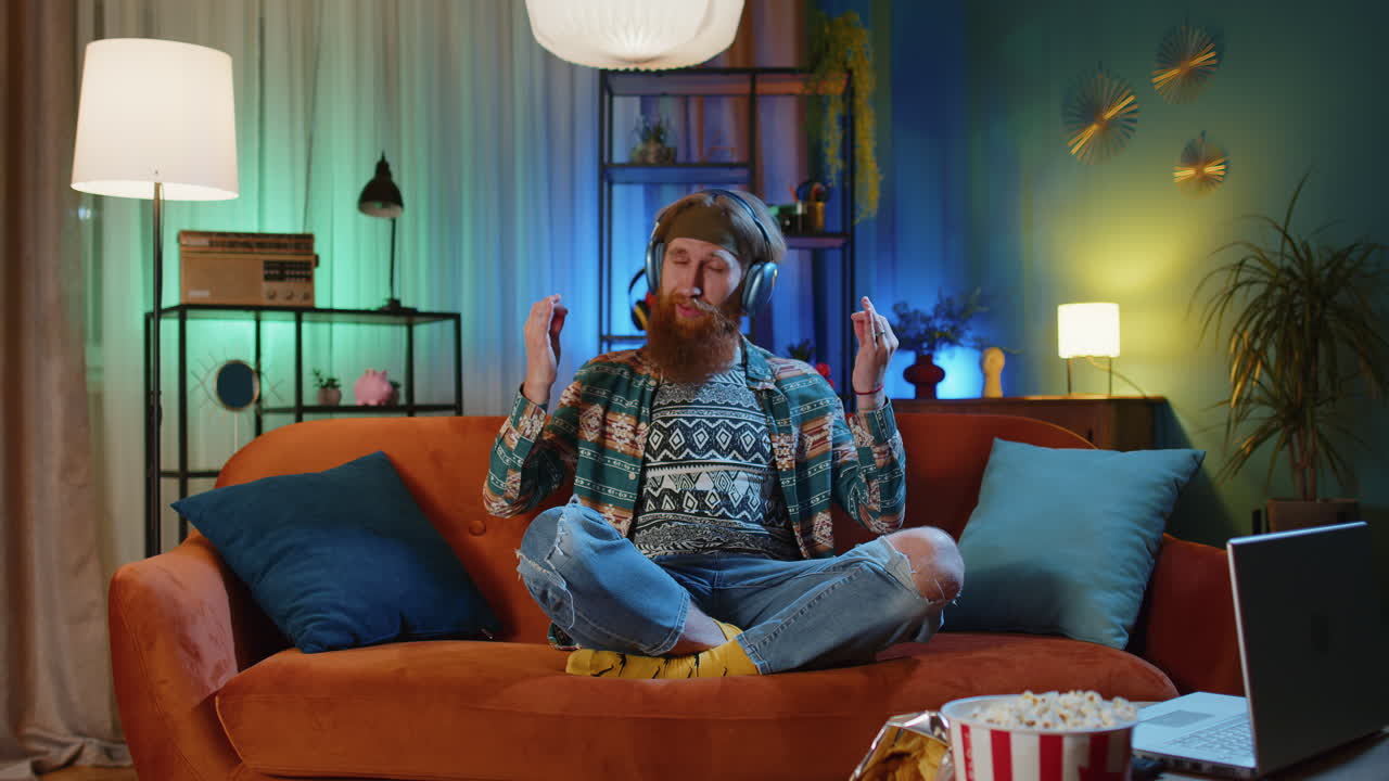 хиппи рыжеволосый мужчина дома на диване с закрытыми глазами медитирует с сосредоточенными мыслями, слушает музыку