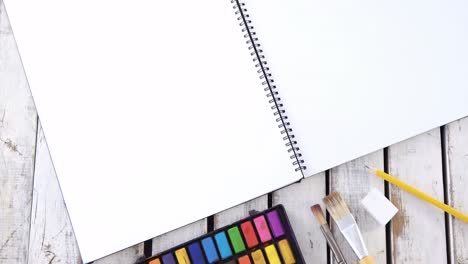 Watercolor-paints-and-paintbrush-with-drawing-book-on-wooden-table