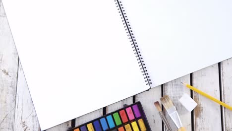 pinturas de acuarela y pincel con libro de dibujos en una mesa de madera