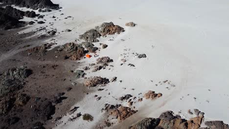 Flyover:-Lone-camper-with-orange-tent-on-remote-sandy-beach-in-Chile