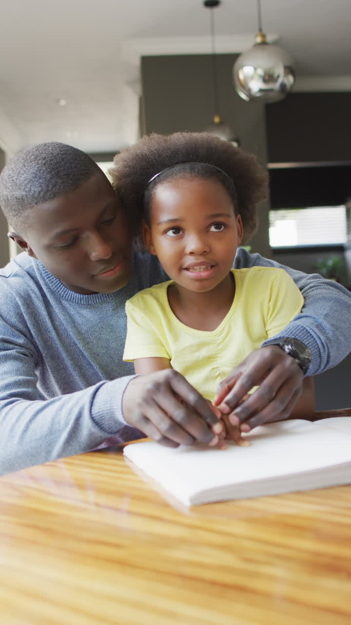 Vertical video of african american father and daughter with sight disability reading braille