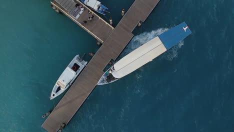 Aerial-top-down-of-departing-tourist-boat-at-pier-of-Gili-Air-during-sunset