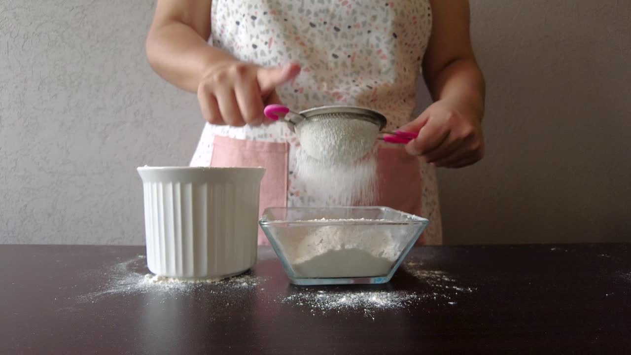 mujer latina con un delantal preparando la cocina horneando un pastel tamizando la harina con un colador de metal y su mano
