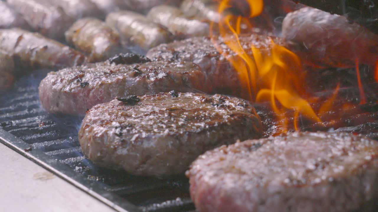 Flames on BBQ Cooking Pepper Seasoned Beef Burgers Outside on Hot Summer Day. Meat Cooked on Iron Grill Outdoors. High Protein Classic Party Food.