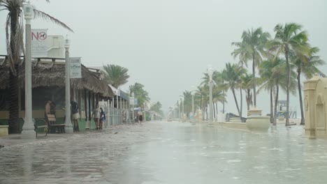 Tropical-Storm,-People-walk-by-on-the-empty-beach-on-a-windy-and-rainy-day