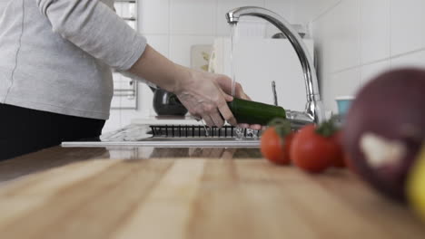 Toma-En-Cámara-Lenta-Como-Una-Mujer-Lavando-Verduras,-Pepino-En-La-Cocina-Con-Agua-Del-Grifo