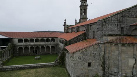 aerial dolly to old weathered stone and orange roof of santa maria de xunqueira monastery