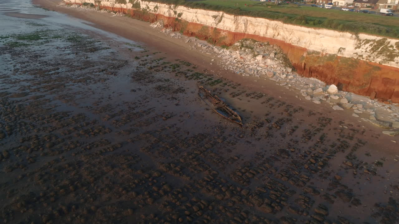 toma aérea de drones del naufragio del barco de arrastre de vapor sheraton antiguo naufragio con bandas naranjas y blancas viejos acantilados de hunstanton y faro al atardecer en el norte de norfolk reino unido