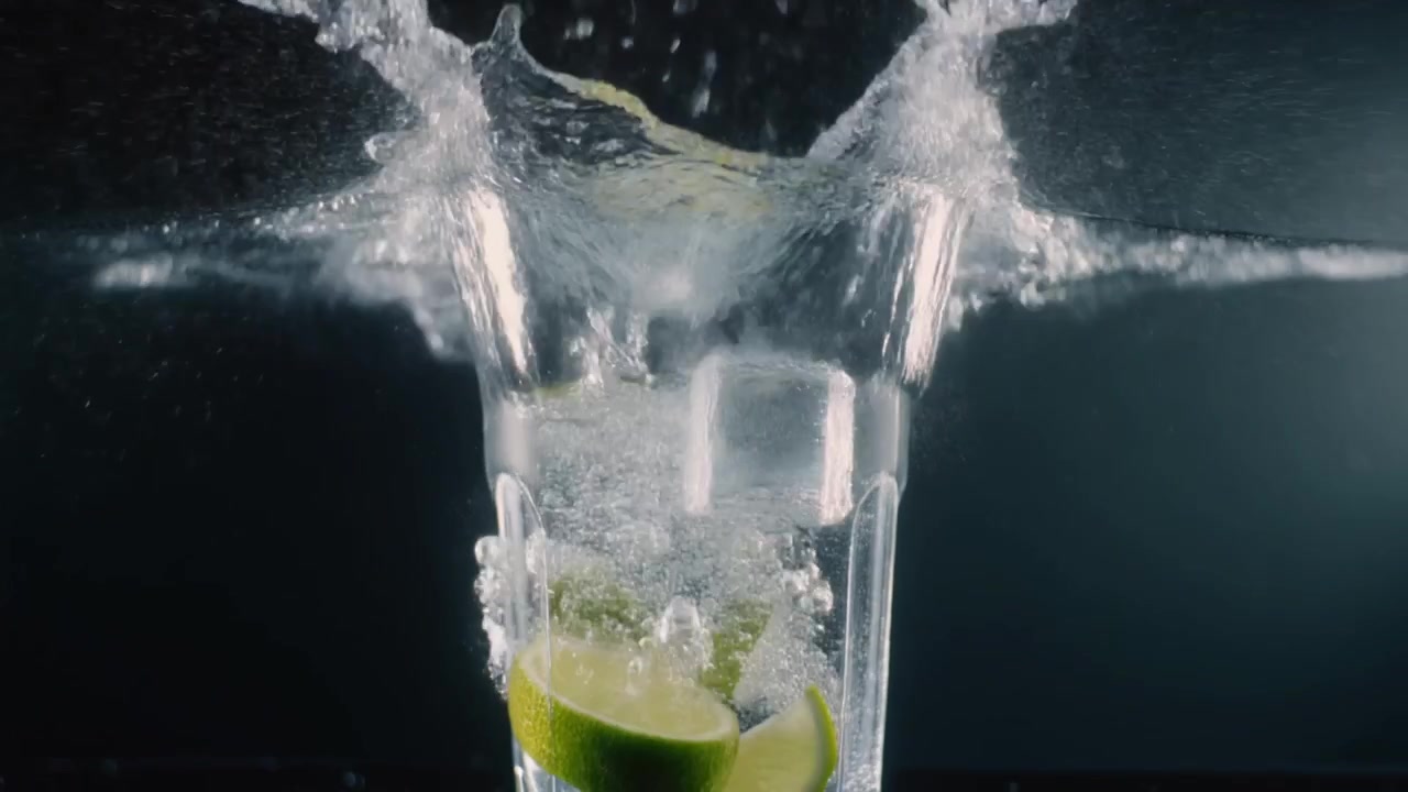 Fette di lime e cubetti di ghiaccio che cadono in un bicchiere d'acqua frizzante