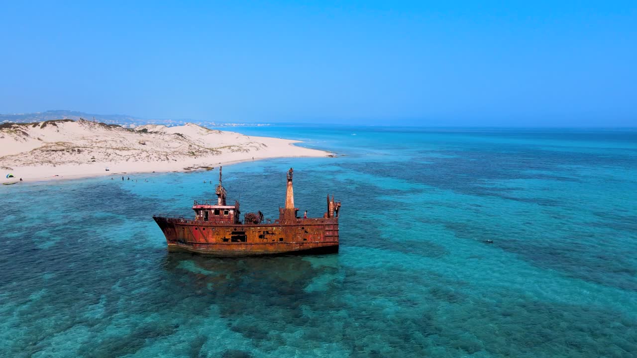 A weathered shipwreck rests peacefully in the shallow, turquoise waters of a serene coastal landscape, offering a striking contrast between decay and natural beauty.