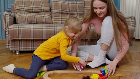 Mother-playing-with-child-kid-daughter-riding-toy-train-on-wooden-railroad-blocks-board-game-at-home