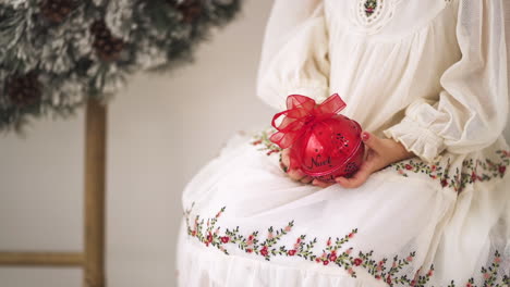 slow motion shot of girl in a christmas holiday festive dress holding a red ornament bauble