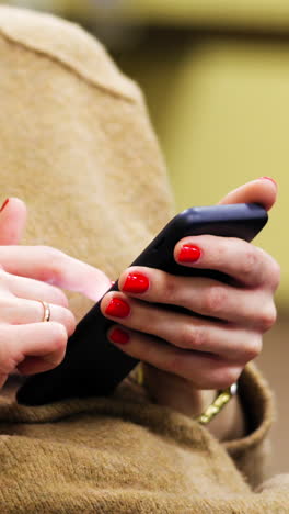 woman in sweater is holding a smartphone in the hands. female hands with red nails typing mobile message on screen smartphone. vertical video