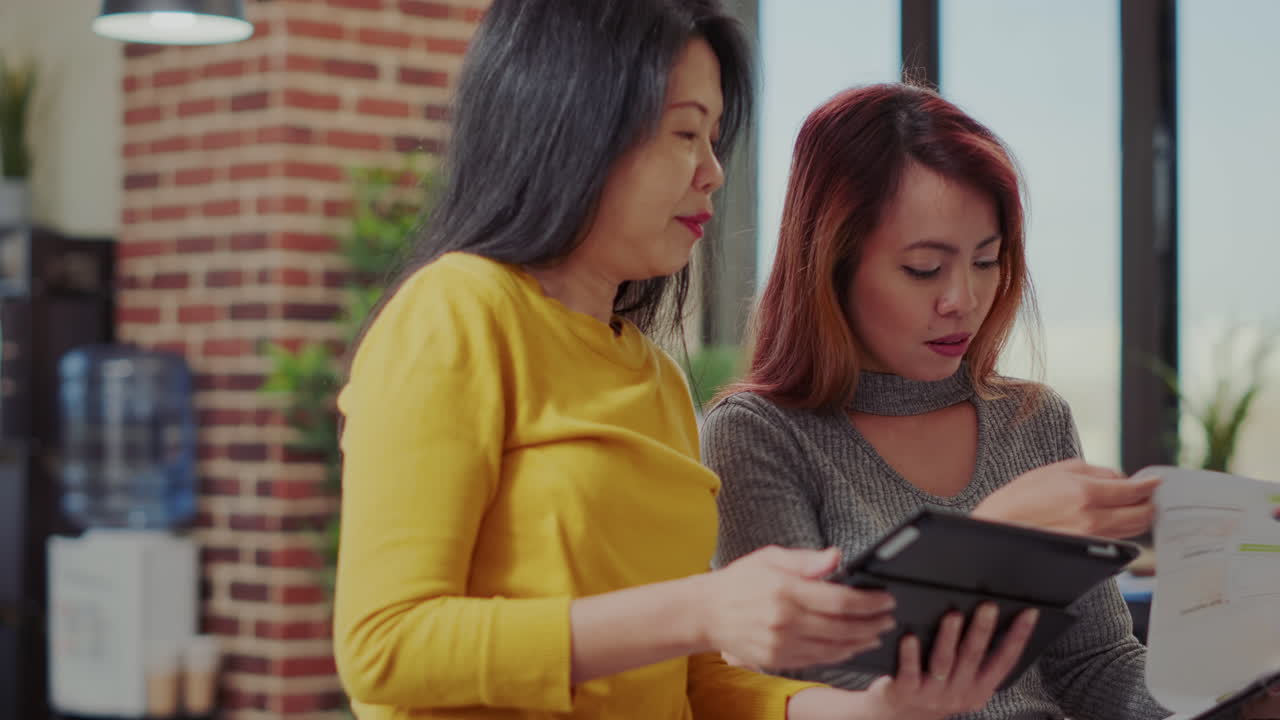 Team of asian women analyzing tablet and paperwork