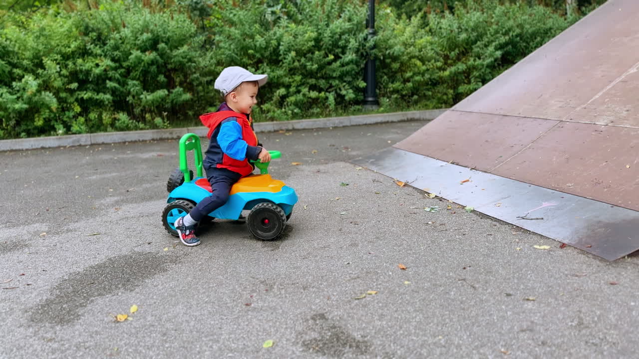 Joyful kid on the toy car tries to get on the slide. Baby boy on the sports ground outdoors.