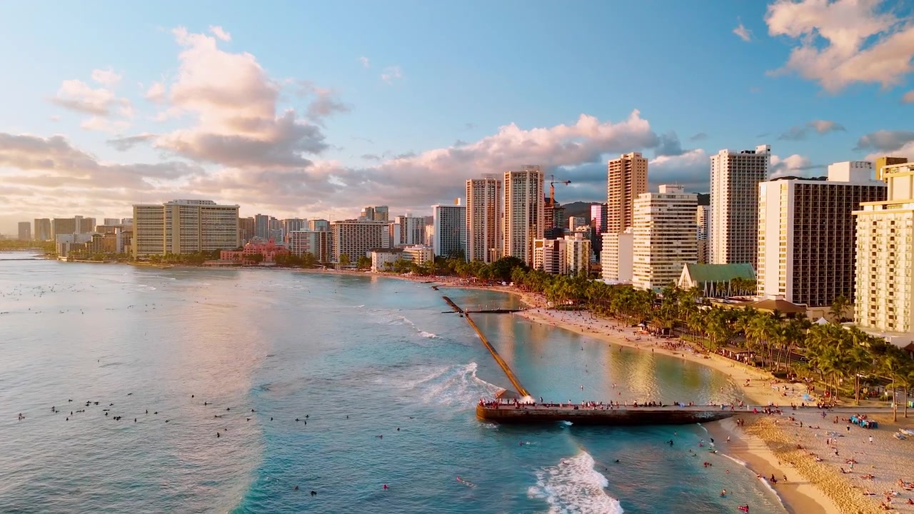 Veduta aerea della spiaggia di Waikiki con surfista, Honolulu, Hawaii. Onda turchese, riva sabbiosa, molo e torre di hotel all'ora d'oro