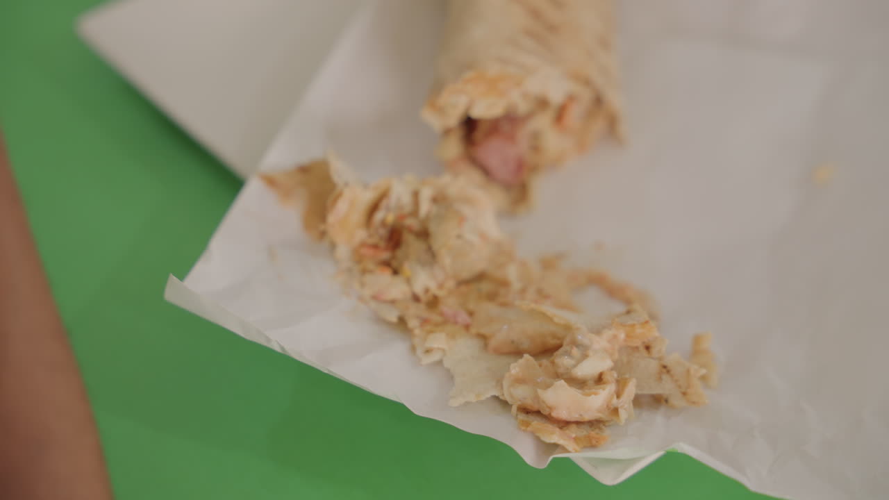 Messy wrap on green table, closeup hand picking torn pita on paper intimate candid moment during casual date, shy laughter, crumbs and sauce textures, soft warm light, relatable food fail