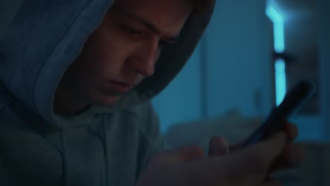 enfoque adolescente caucásico usando teléfono móvil mientras está sentado por la noche en su habitación.