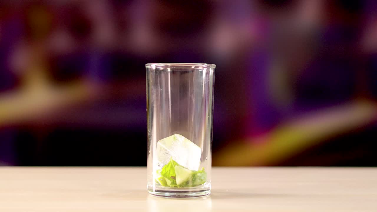 Ice cubes fall into a glass with lime, set against a vibrant background, creating a refreshing cocktail scene