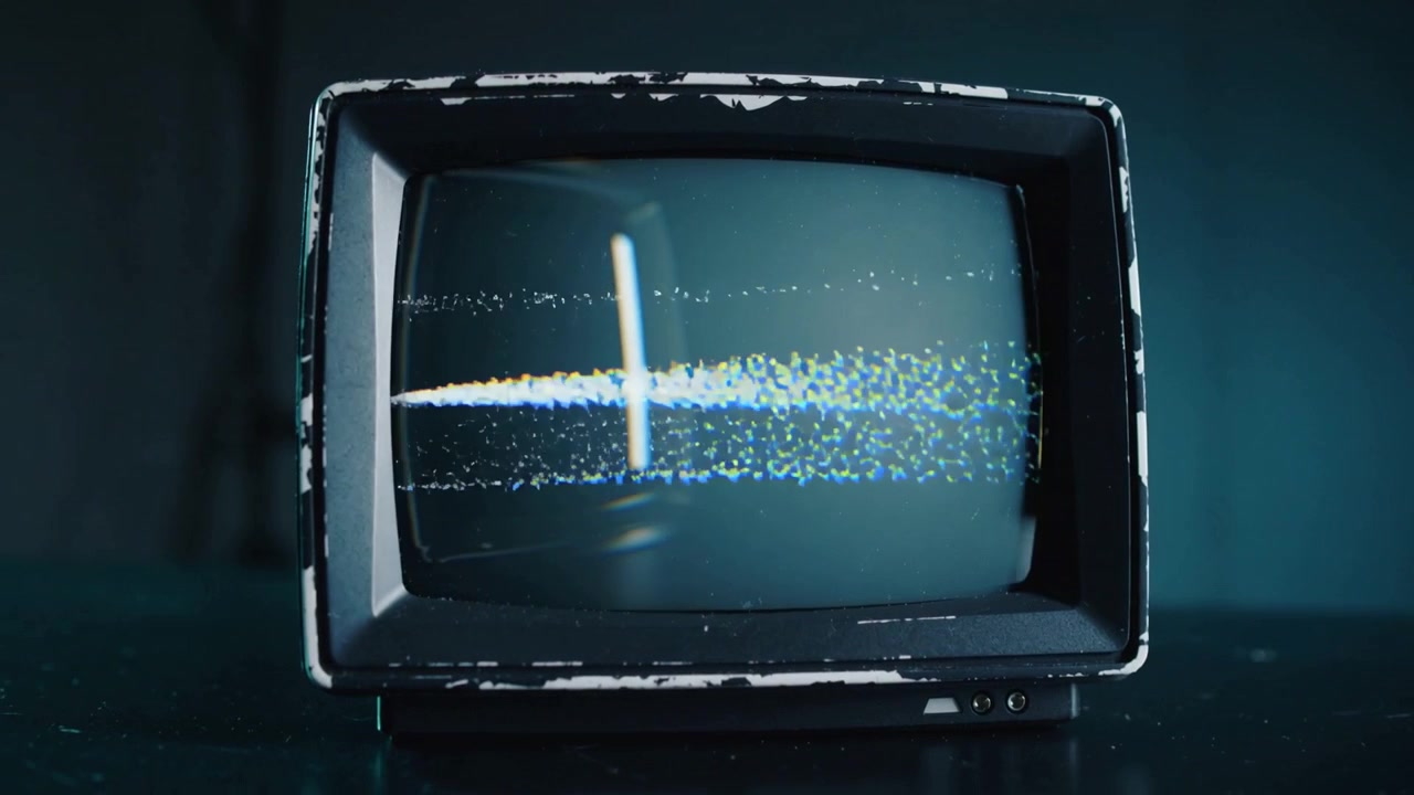 Un monitor CRT vintage mostra una banda di particelle che emerge da sinistra e si muove verso destra su un tavolo color verde acqua, con il cavo di alimentazione.