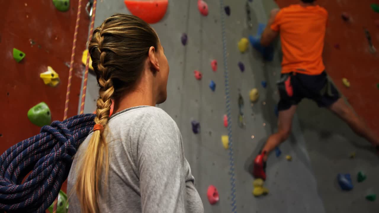 mujer viendo a un hombre escalar una pared artificial 4k