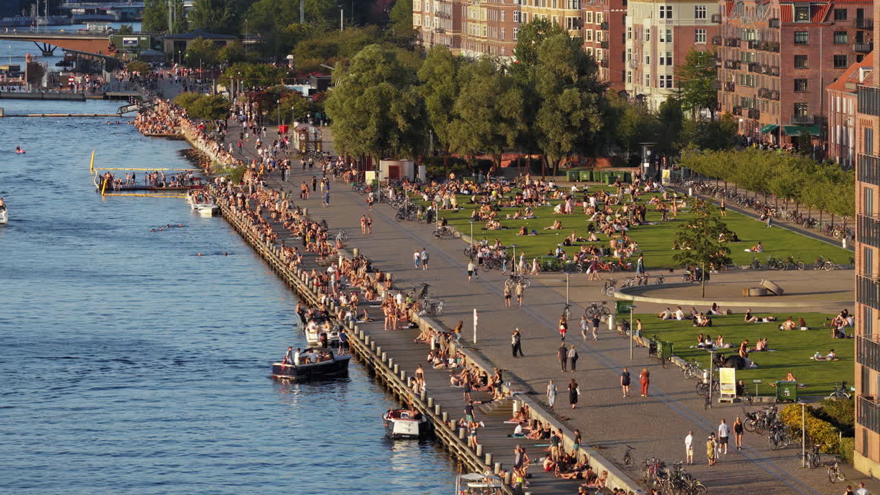 Copenhagen, Denmark - August 6, 2025: Aerial drone view of crowds gathering by the water for swimming, sunbathing, and socialising on a warm evening at Islands Brygge Harbour