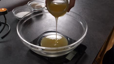 zoom in close up shot of a girl pouring honey into a glass bowl to prepare a honey cake filling