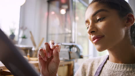 Female-Jeweller-Comparing-Ring-With-Drawn-Design-On-Digital-Tablet-In-Studio