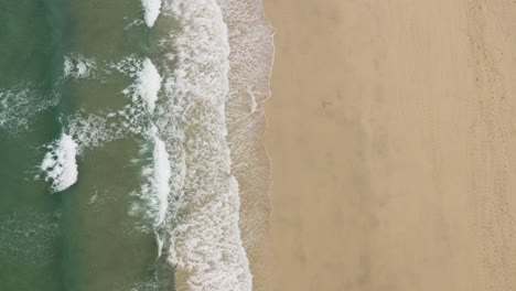 vertical shot of foamy waves washed over sandy shore at st ives, cornwall, england