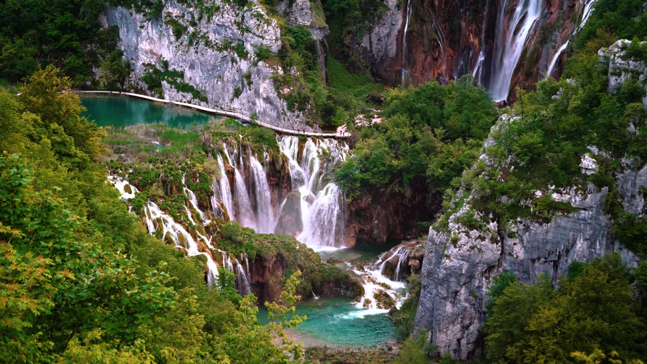 Multiple waterfalls flowing into turquoise clear water lake in Plitvice Lakes National Park, Croatia